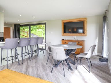 A dining area with round table and four chairs and a bar counter with four high stools next to sliding glass doors at Orchard Lodge in Maerdy near Corwen