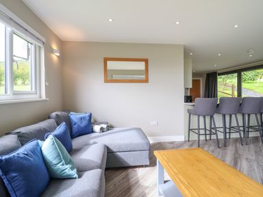 A living room with a gray sectional sofa with blue cushions a wooden coffee table and bar stools at Orchard Lodge in Maerdy near Corwen