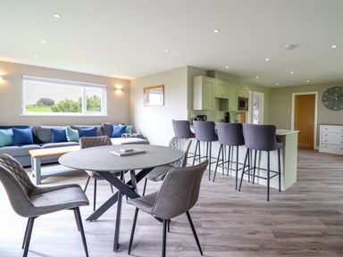 A living area with a round dining table and chairs a kitchen island with bar stools and a sofa near a window at Orchard Lodge Maerdy near Corwen