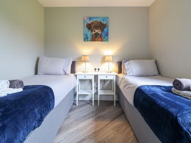 A bedroom with two single beds with blue blankets and white bedside table with lamps at Orchard Lodge Maerdy near Corwen