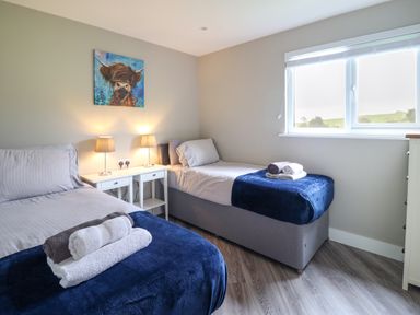 A bedroom with two single beds with blue blankets and rolled towels lamps on a small white table and a window at Orchard Lodge in Maerdy near Corwen