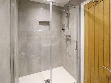 A shower area with glass doors a shower head and a wooden door at Orchard Lodge in Maerdy near Corwen
