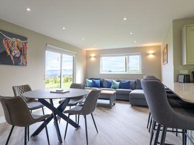 A dining area with a round table and four chairs next to a living area with a sectional sofa and a coffee table at Orchard Lodge in Maerdy near Corwen