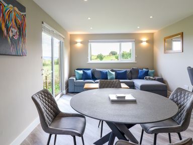 A dining area with a round table and four chairs next to a living room with a sofa and colorful cushions at Orchard Lodge in Maerdy near Corwen