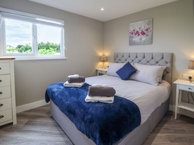 A bedroom with a double bed blue throws and towels bedside tables with lamps and a painting at Orchard Lodge Maerdy near Corwen
