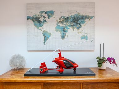 A wooden table with a red model helicopter a decorative silver object and a potted orchid below a world map on the wall at Howard Cottage in North Littleton near Offenham