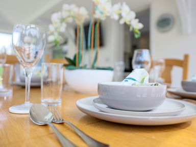 A dining table set with plates bowls glasses utensils and a flower centerpiece at Howard Cottage in North Littleton near Offenham