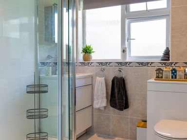 A bathroom with a glass shower enclosure towels hanging on rings and decorative items on the window sill at Howard Cottage in North Littleton near Offenham