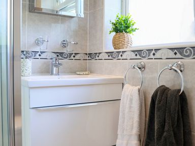 A bathroom sink with a faucet a small plant on the window ledge and two towels hanging on rings at Howard Cottage in North Littleton near Offenham