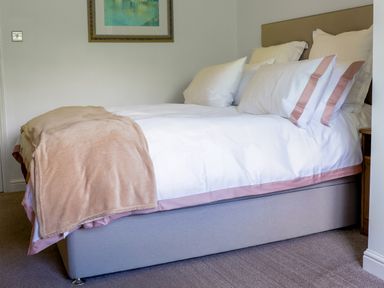 A bedroom with a bed with white and pink bedding and a beige throw at Howard Cottage North Littleton near Offenham