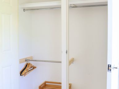 A closet with white sliding doors wooden hangers on a metal rod and a wooden shoe rack at Howard Cottage in North Littleton near Offenham