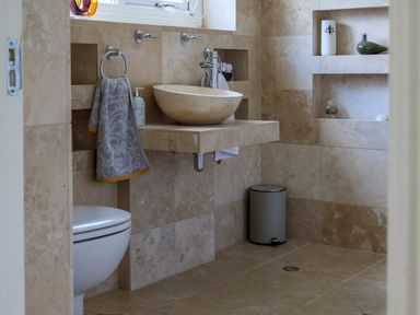 A bathroom with a wall-mounted sink a toilet a towel on a ring and shelves with decorative items at Howard Cottage in North Littleton near Offenham