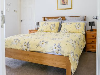 A bedroom with a wooden bed frame and yellow floral bedding between two wooden bedside tables at Howard Cottage in North Littleton near Offenham
