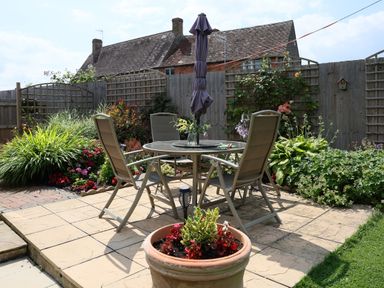A patio with a round table and four chairs an umbrella in the center and potted plants around at Howard Cottage in North Littleton near Offenham