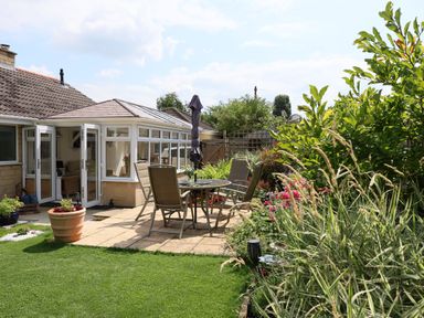 A backyard patio with a glass table and four chairs next to a conservatory at Howard Cottage in North Littleton near Offenham