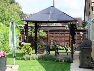 A backyard with a gazebo table and chairs a barbecue and plants at Howard Cottage in North Littleton near Offenham
