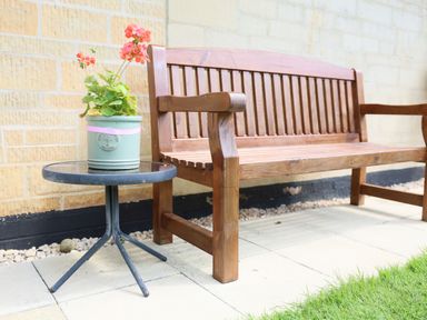 A wooden bench and a small round table with a flowerpot on a patio at Howard Cottage in North Littleton near Offenham