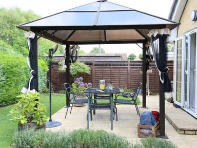 A garden patio with a table and four chairs under a gazebo at Howard Cottage in North Littleton near Offenham