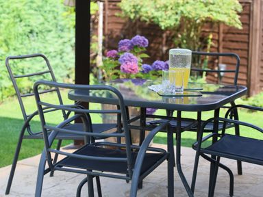 An outdoor patio with a glass table and four metal chairs with a pitcher of yellow drink and two glasses at Howard Cottage North Littleton near Offenham