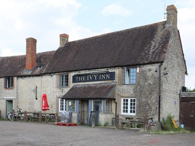 The exterior of a stone building with a sign reading The Ivy Inn and outdoor seating at Howard Cottage in North Littleton near Offenham