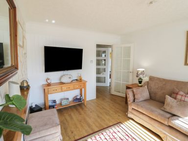 A living room with a sofa a television on the wall a wooden console table and a lamp at Howard Cottage in North Littleton near Offenham