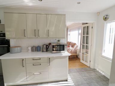 A kitchen with beige cabinets a microwave kettle and canisters with a view into a sitting area at Howard Cottage in North Littleton near Offenham