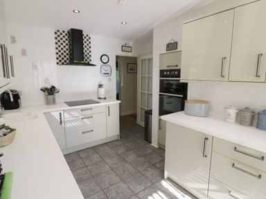 A kitchen with white cabinets gray tiled floor stove oven and countertop containers at Howard Cottage North Littleton near Offenham