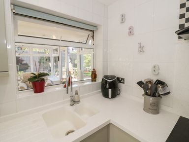 A kitchen sink with a red potted plant and utensils on the countertop at Howard Cottage in North Littleton near Offenham