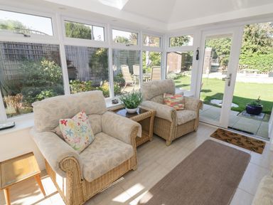 A conservatory with two armchairs and a small table inside with a garden visible outside at Howard Cottage in North Littleton near Offenham