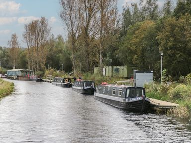 A canal with narrowboats moored alongside trees and grass at Aspen in Denny
