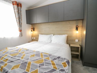 A bedroom with a double bed two pillows wall lamps wooden headboard and grey and orange curtains at Elm in Denny