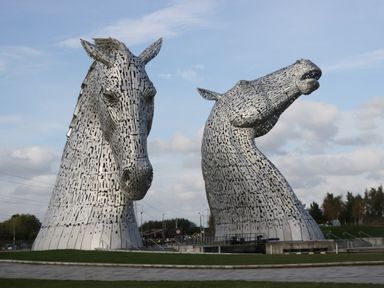 Two large metal horse head sculptures outdoors with grass and cloudy sky at Elm in Denny