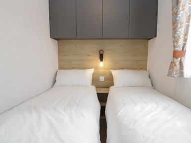 A bedroom with two single beds a wooden headboard and wall-mounted cabinets at Elm in Denny