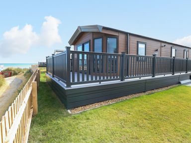An exterior view of a wooden lodge with a glass railing deck and grass surrounding the property at Seaview Lodge in Bacton