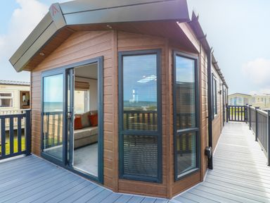 Exterior view of a wooden lodge with large windows and a deck with railing at Seaview Lodge in Bacton
