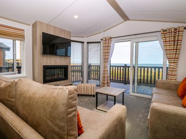 A living room with two sofas a wall-mounted television a fireplace a small table and sliding glass doors leading to a balcony at Seaview Lodge in Bacton