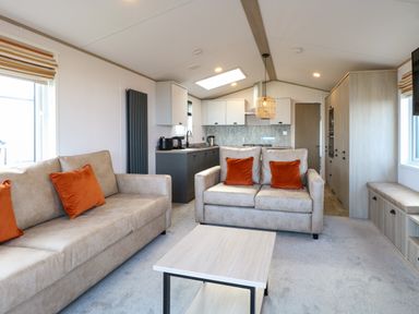 A living room with two beige sofas with orange cushions and a coffee table in front at Seaview Lodge in Bacton