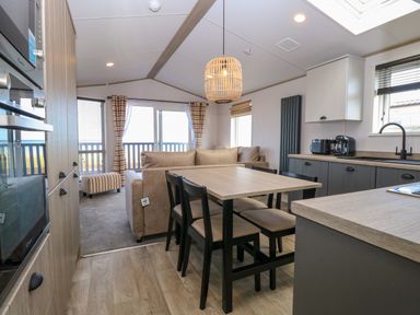 A kitchen and dining area with a wooden table and chairs a beige sofa and sliding glass doors leading to a balcony at Seaview Lodge in Bacton