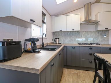 A kitchen with a toaster coffee machine sink and gas stove with cabinets and a chair at Seaview Lodge in Bacton