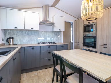 A kitchen with a wooden dining table black chairs gray and white cabinets and built in oven and microwave at Seaview Lodge in Bacton