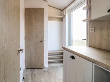 A utility room with wooden doors a countertop a coat rack with hooks and a frosted glass door at Seaview Lodge in Bacton