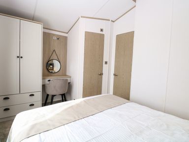 A bedroom with a bed a wardrobe a small desk with a chair and a round mirror at Seaview Lodge in Bacton
