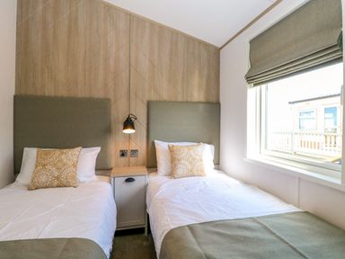 A bedroom with two single beds a small cabinet and a window with a blind at Seaview Lodge in Bacton