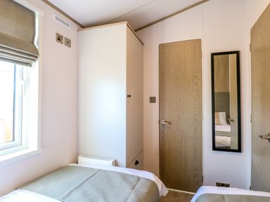 A bedroom with two single beds a white wardrobe a wooden door and a mirror on the wall at Seaview Lodge in Bacton