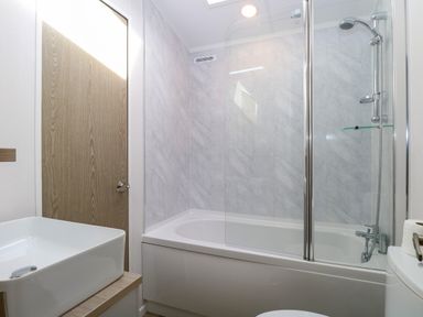 A bathroom with a bathtub shower combination a wooden door and a white sink at Seaview Lodge in Bacton