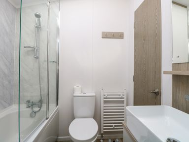 A bathroom with a bathtub and shower, toilet with a roll of toilet paper, towel radiator, wooden door, and a sink at Seaview Lodge in Bacton
