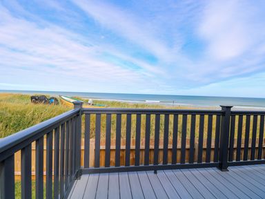 A deck with black railing overlooking grass dunes and a beach with boats at Seaview Lodge in Bacton