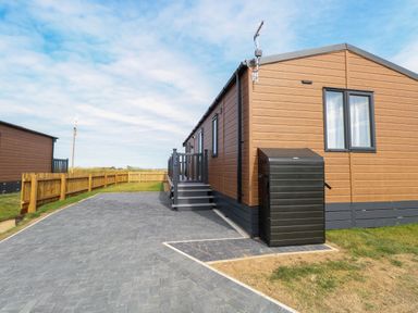 An exterior view of a brown mobile home with a small deck and stairs on a paved driveway with a wooden fence on the side at Seaview Lodge in Bacton