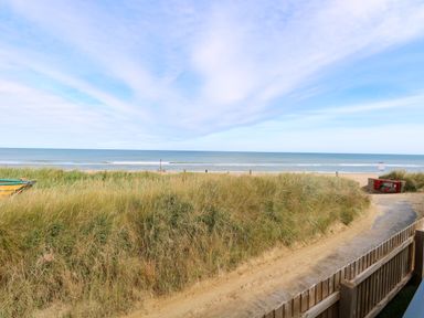 A sandy path leading to a beach with grass dunes and the ocean in the background at Seaview Lodge in Bacton