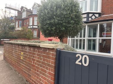 A residential street with brick houses a gray gate with number 20 and a tree at Happy Place in Sheringham